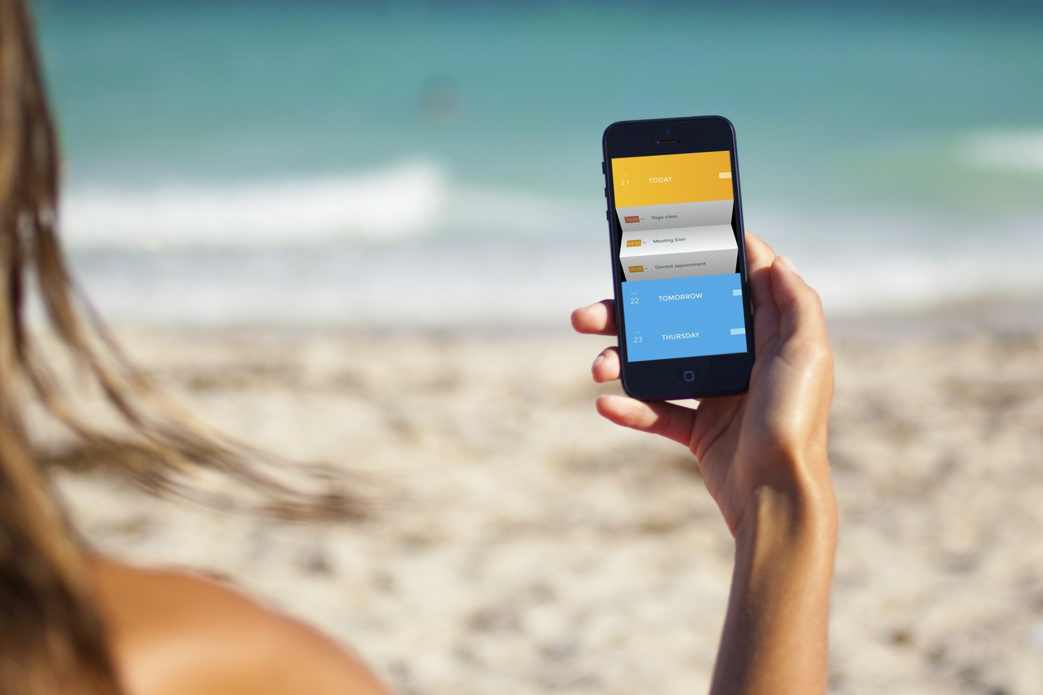 Woman on a beach checking Peek Calendar on her iPhone