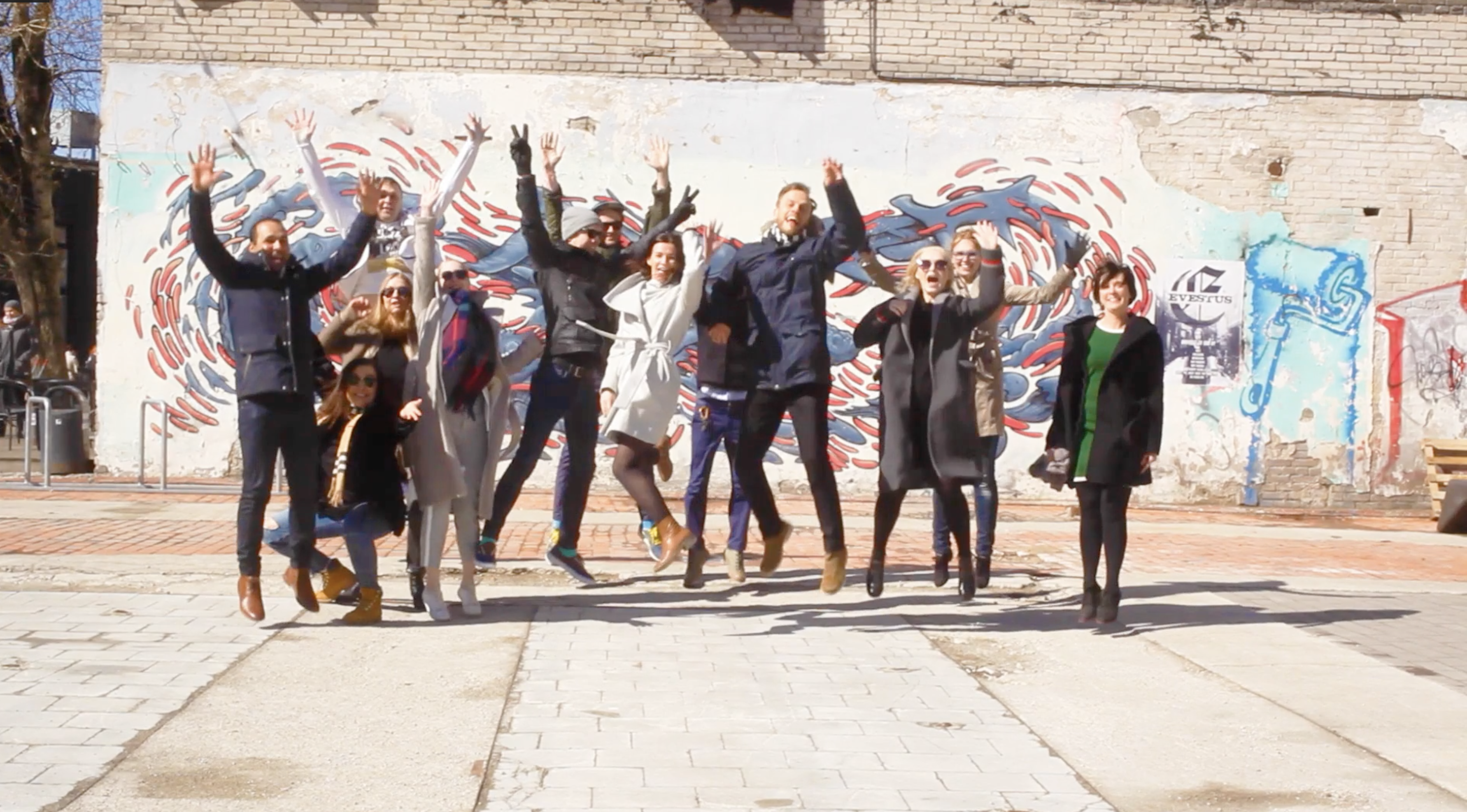 A group of IxD.ma students jumping in celebration in front of a mural