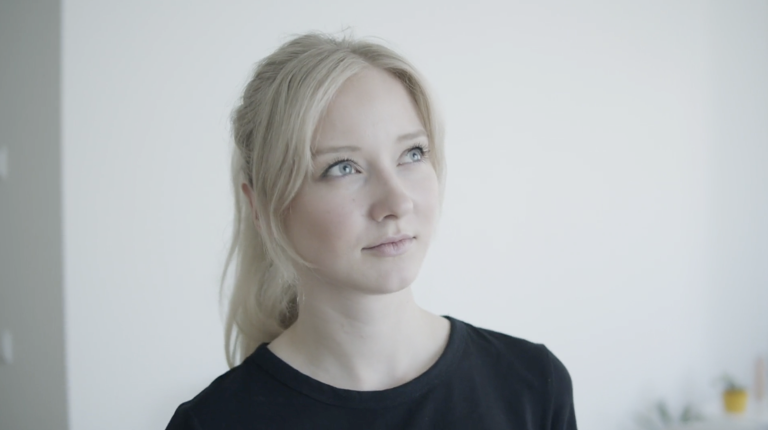 A woman in a black t-shirt looking off to the side in a bright, minimal room