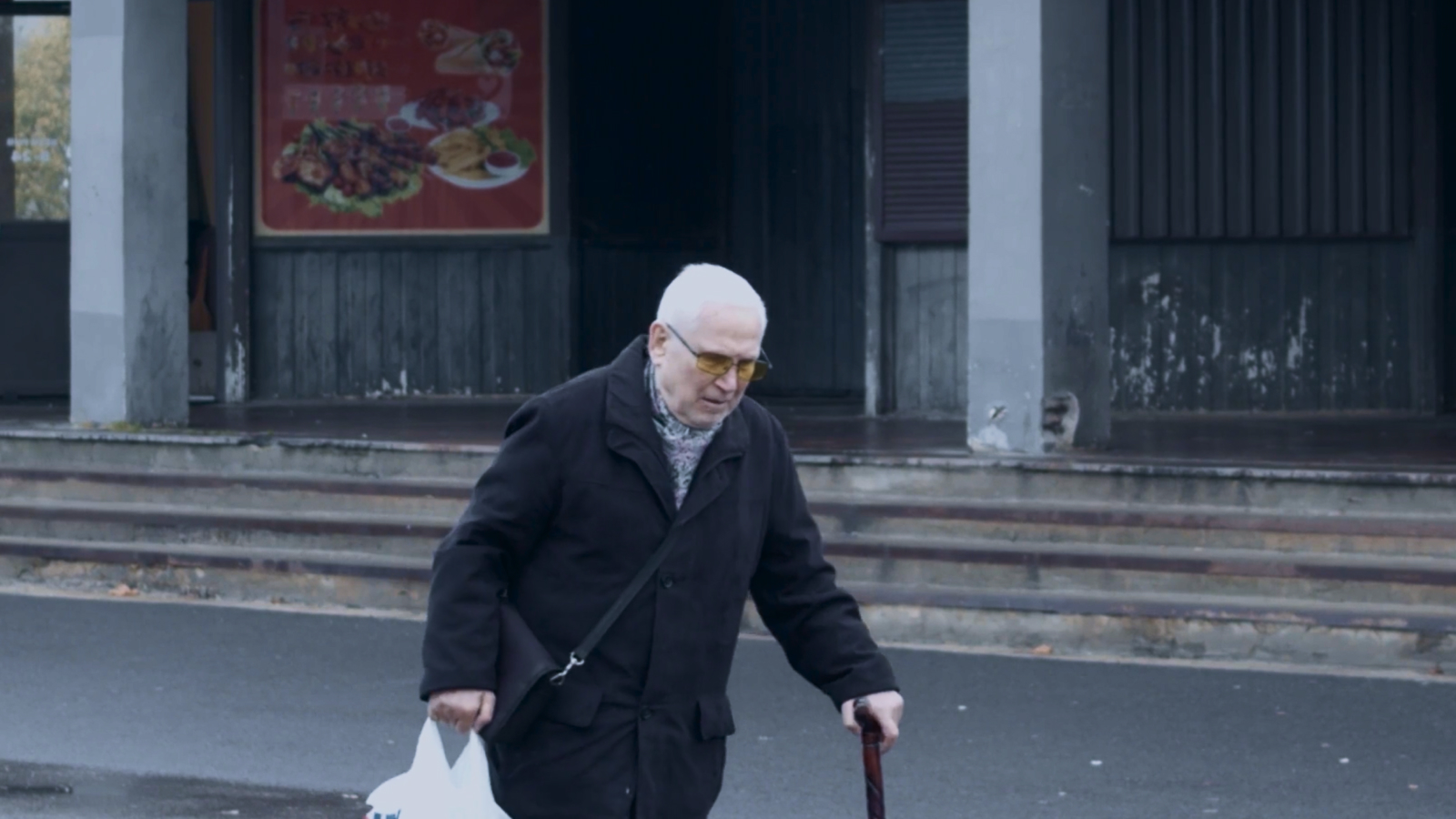 An elderly man walking with a cane past a building in Lasnamäe