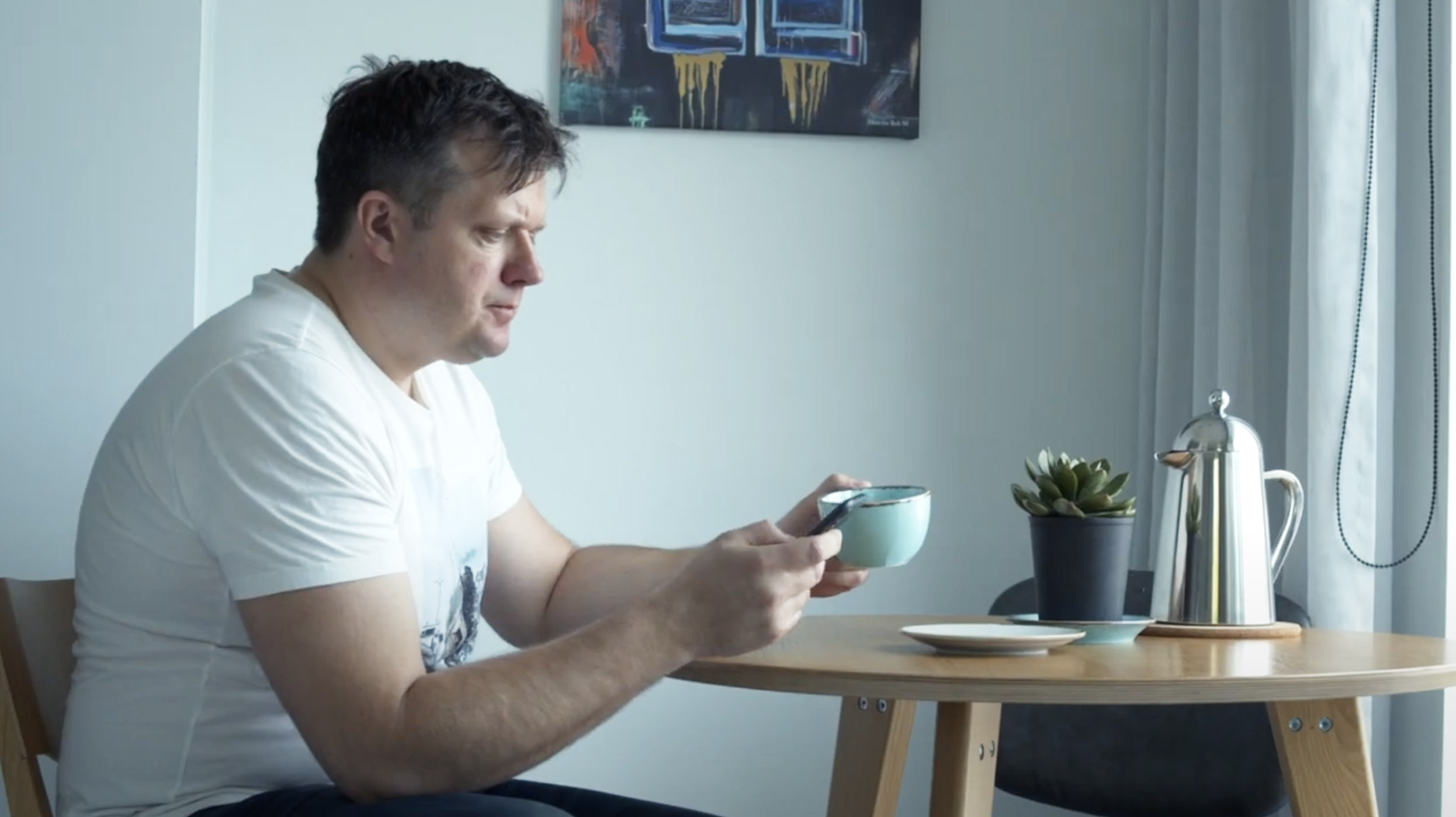 A man checking his phone while having coffee at a table